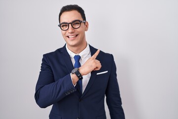 Young hispanic man wearing suit and tie cheerful with a smile of face pointing with hand and finger up to the side with happy and natural expression on face
