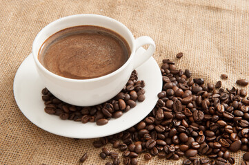 Cup of coffee on a saucer with coffee beans on a background of burlap
