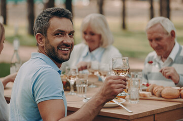 Happy young man cheering with glass of wine while having family dinner outdoors