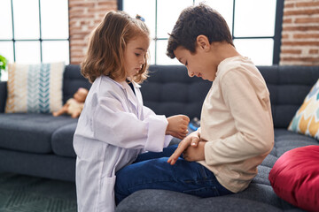 Adorable boy and girl wearing doctor uniform examining with stethoscope at home