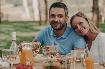 Happy young couple looking at camera while enjoying dinner outdoors together