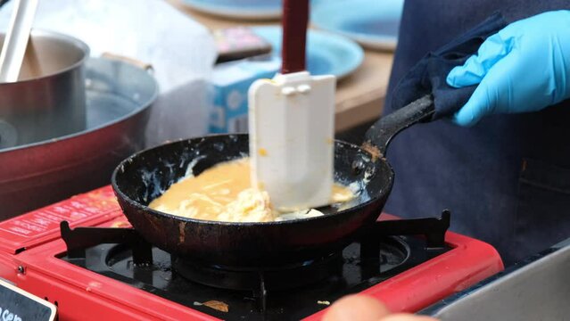 A cook is using a plastic spatula to make an omelet in a pan.