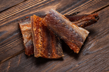 Pieces of cleaned dried fish on wooden background. Dry Peppered Pollack. Amber with pepper