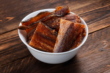 Pieces of cleaned dried fish in the bowl on wooden background. Dry Peppered Pollack. Amber with pepper