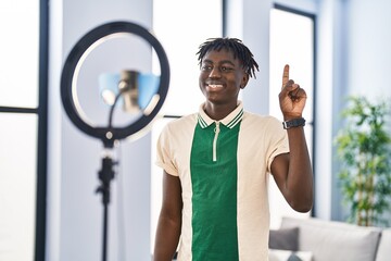 African man with dreadlocks recording vlog tutorial with smartphone at home smiling with an idea or...