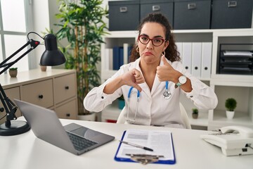 Young hispanic woman wearing doctor uniform and stethoscope doing thumbs up and down, disagreement and agreement expression. crazy conflict