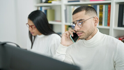 Man and woman students using computer talking on smartphone at university classroom
