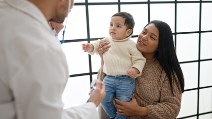 Couple and son examining baby with stethoscope at clinic