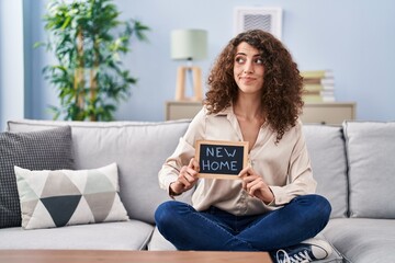 Obraz premium Hispanic woman with curly hair sitting on the sofa at new home smiling looking to the side and staring away thinking.