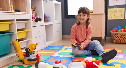 Adorable hispanic girl playing supermarket game sitting on floor at kindergarten