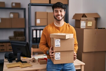 Hispanic man with beard working at small business ecommerce holding packages smiling with a happy and cool smile on face. showing teeth.
