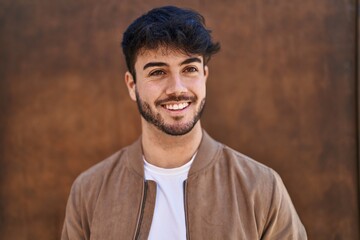 Young hispanic man smiling confident looking to the side over brown isolated background