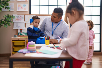 Fototapeta premium Hispanic man and group of kids playing telephone toy standing at kindergarten