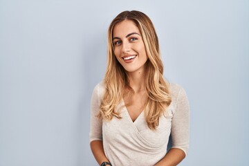 Young blonde woman standing over isolated background with hands together and crossed fingers smiling relaxed and cheerful. success and optimistic