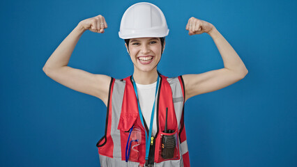 Young beautiful hispanic woman builder smiling confident doing strong gesture over isolated blue...