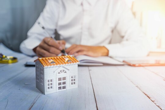 Small House Model On The Desk In Front Of The Realtor - Real Estate Concept