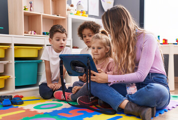 Woman and group of kids having lesson using touchpad at kindergarten - obrazy, fototapety, plakaty