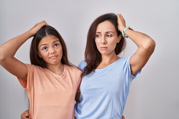 Young mother and daughter standing over white background confuse and wondering about question....