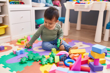 Adorable hispanic boy playing with crocodile toy sitting on floor at kindergarten