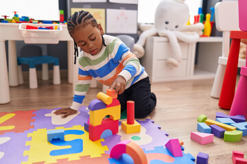 African american boy playing with construction blocks sitting on floor at kindergarten
