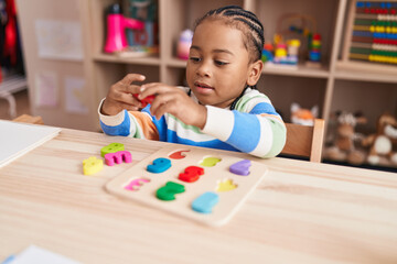 African american boy playing with maths puzzle game sitting on table at kindergarten