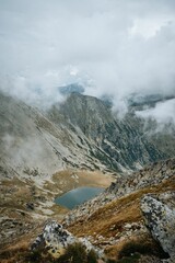 Vertical shot of a rocky mountain landscape with small lake in the middle in fog