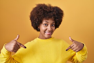 Young african american woman standing over yellow background looking confident with smile on face,...