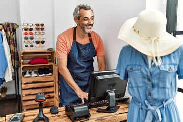 Middle age grey-haired man shop assistant using computer working at clothing store