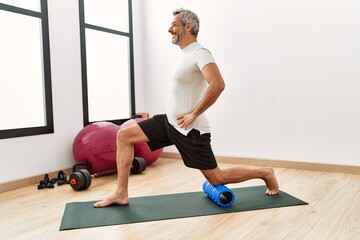 Middle age grey-haired man using foam roller stretching at sport center