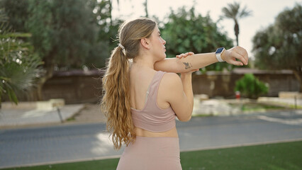 Young blonde woman wearing sportswear stretching arms at park