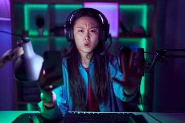 Young asian woman playing video games with smartphone doing stop gesture with hands palms, angry and frustration expression