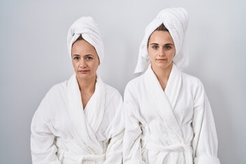 Middle age woman and daughter wearing white bathrobe and towel relaxed with serious expression on face. simple and natural looking at the camera.