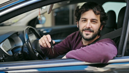 Young hispanic man smiling confident holding key of new car at street