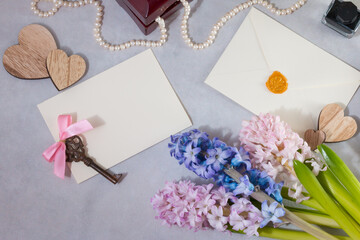 Romantic love letters concept. Pink and blue hyacinth, with the wooden hearts and white card on light gray background.