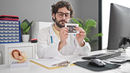 Young hispanic man gynecologist holding baby ecography at clinic