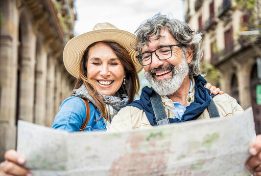Married couple of tourists sightseeing city street with map - Happy husband and wife enjoying summer vacation together - Touristic life style concept with aged woman and man traveling European city
