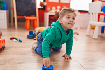 Adorable caucasian boy playing with car toy sitting on floor at kindergarten