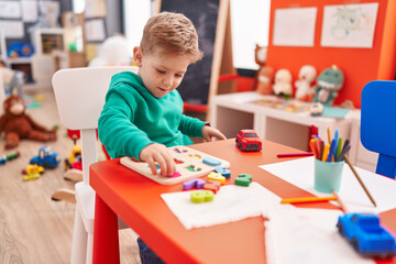 Fototapeta premium Adorable caucasian boy playing with maths puzzle game sitting on table at kindergarten