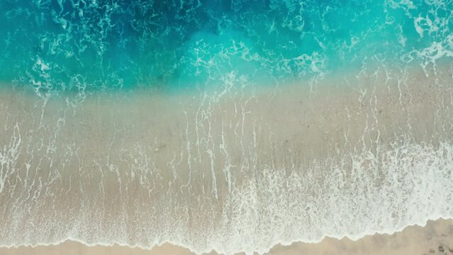 Aerial top view of ocean turquoise blue waves break on a beach. Aerial shot of beach with small stones meeting ocean water and foam. Top view of paradise island. tidal wave floods sandy beach. relax.