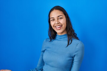 Fototapeta premium Young brazilian woman standing over blue isolated background smiling cheerful with open arms as friendly welcome, positive and confident greetings