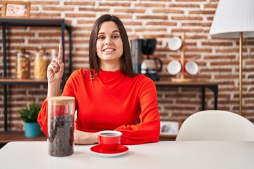Young hispanic woman drinking coffee at home surprised with an idea or question pointing finger with happy face, number one