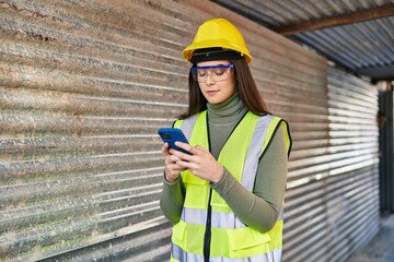 Young beautiful hispanic woman architect using smartphone at street