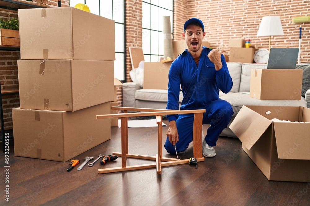 Sticker Young hispanic man working on moving service pointing thumb up to the side smiling happy with open mouth