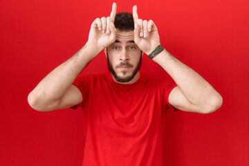 Naklejka premium Young hispanic man wearing casual red t shirt doing funny gesture with finger over head as bull horns