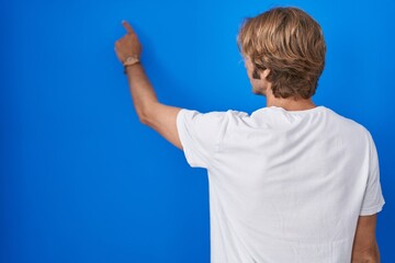 Middle age man standing over blue background posing backwards pointing ahead with finger hand