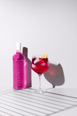 Refrescante gin tónica rosa decorado con naranja sobre un fondo con sombras	