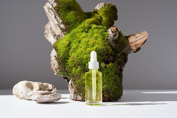 Botella de aceite esencial con cuentagotas sobre un tronco de árbol con musgo	