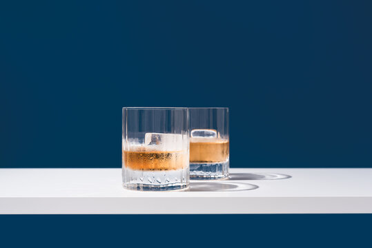Dos vasos de whisky con hielo sobre un fondo azul