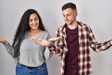 Young hispanic couple standing over white background smiling showing both hands open palms,...