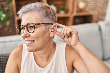 Middle age woman using hearing aid sitting on sofa at home